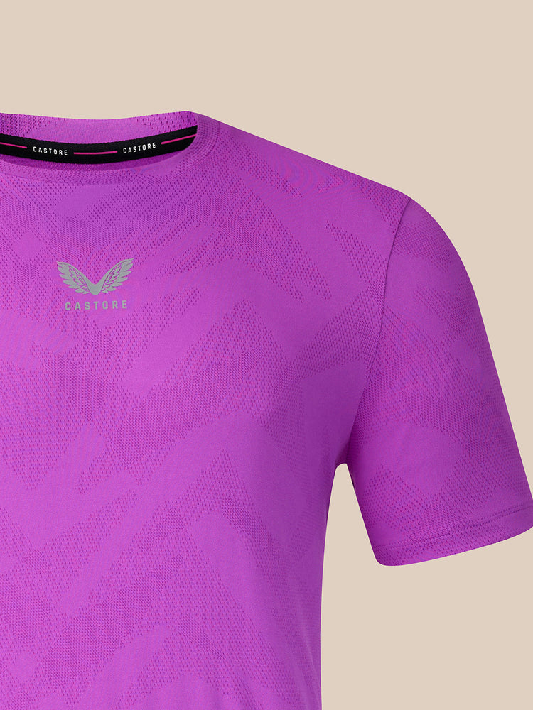 Close-up of a purple short-sleeve athletic t-shirt with a subtle geometric pattern, featuring a light gray winged logo and the brand name 'CASTORE' printed on the chest and inner neck label.