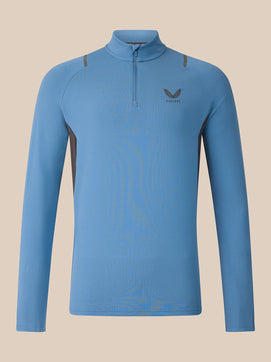 A light blue long-sleeve quarter-zip athletic top with a small dark gray wing logo and the brand name 'CASTORE' on the left chest, displayed against a solid beige background.